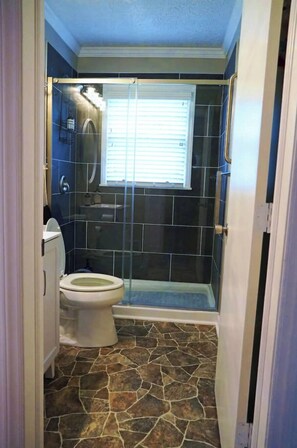 A bathroom with a toilet, a shower enclosure, and a tiled floor.