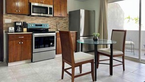 Une cuisine moderne avec des meubles en bois, un four à micro-ondes, une cuisinière et un réfrigérateur. On y trouve une table en verre avec deux chaises et une plante en pot.