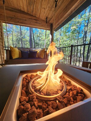 A wooden deck with a fire feature surrounded by rocks, overlooking a forested area. - Rustic Comfort Cabin
Diamond in The Ripple- Hot  (Amity)