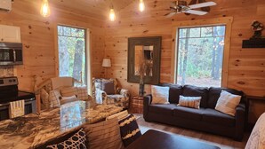 L’intérieur chaleureux d’un chalet, avec un revêtement mural en bois, une table à manger entourée de chaises, un canapé et un ventilateur de plafond.