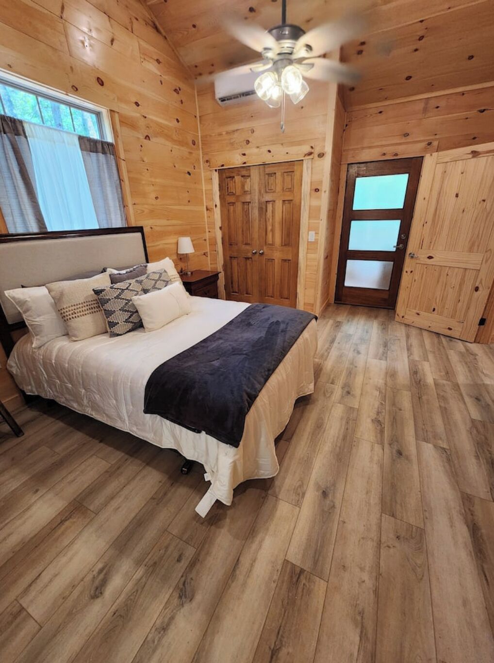 A wooden cabin bedroom with a bed, a ceiling fan, and a door.