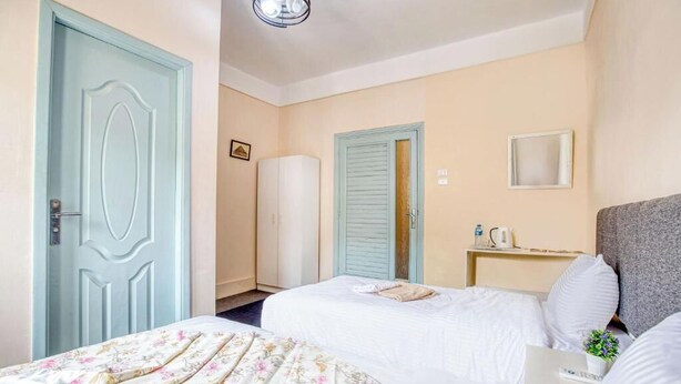 Una camera d'albergo con due letti, un comodino con una lampada, uno specchio piccolo e una mensola a muro con una pianta.