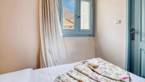 A bedroom with a bed, a window with curtains, and a view of a pyramid. - Deluxe Double or Twin Room with Pyramids View (Giza Governorate)