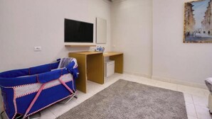 Une chambre avec un berceau, un bureau, une télévision et un tableau accroché au mur.