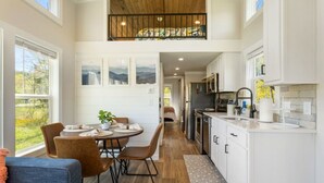 Una cocina moderna con armarios blancos, un comedor con mesa y sillas redondas, y vistas al exterior a través de grandes ventanales.