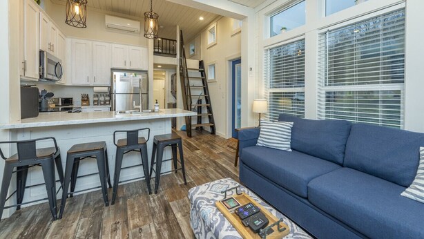 A modern kitchen with a central island, bar stools, and a blue sofa in a living area with large windows.
