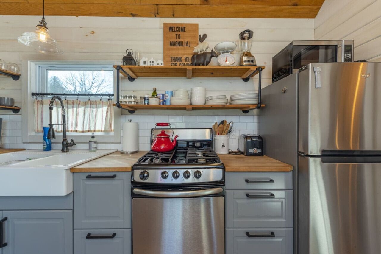 A kitchen with a stainless steel stove, a refrigerator, and wooden shelves above the counter.