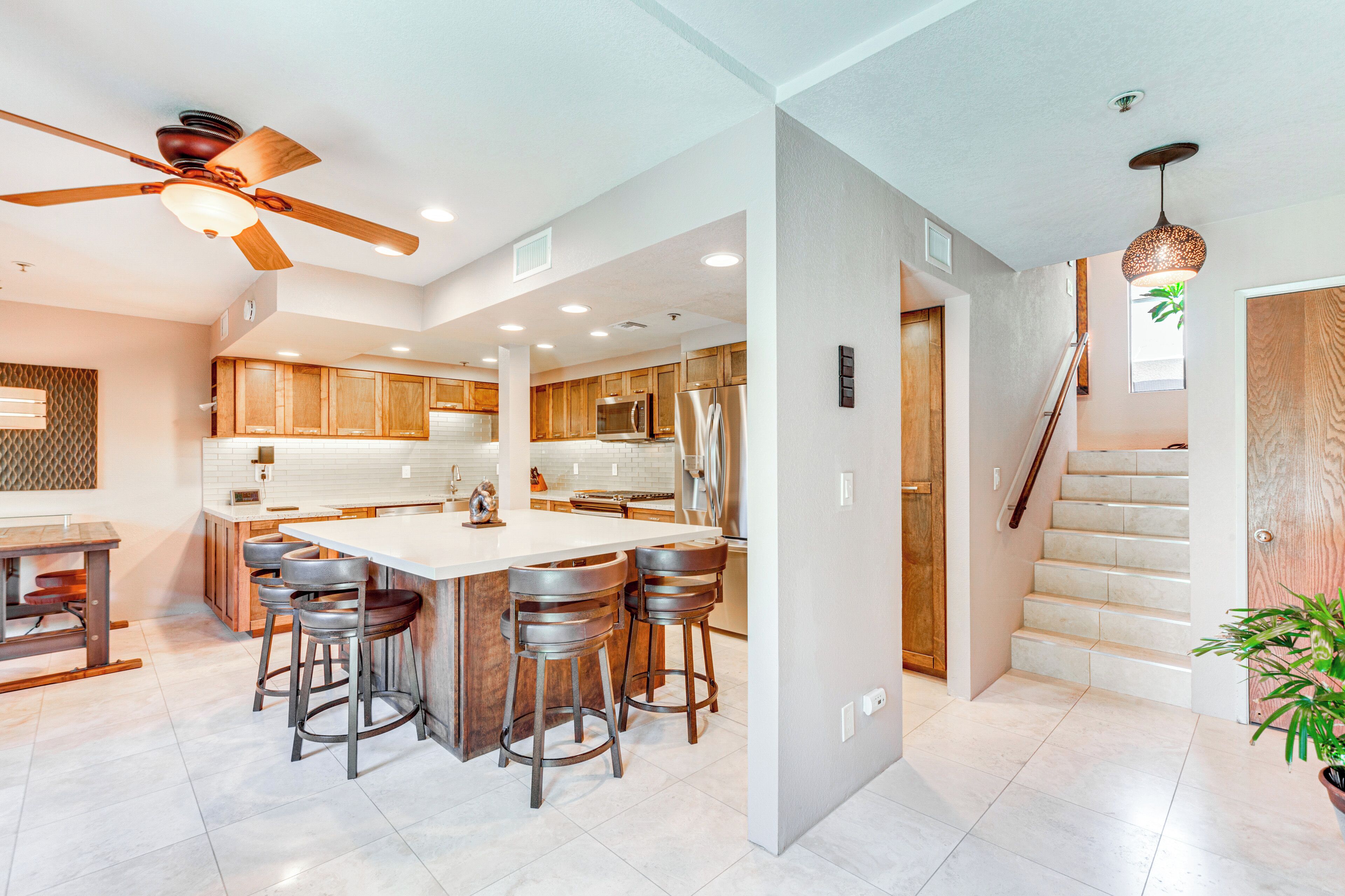 A spacious kitchen with a central island, wooden cabinets, and a ceiling fan.