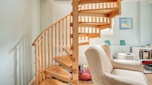 Un escalier en colimaçon en bois dans un salon, avec un fauteuil beige et une bibliothèque.