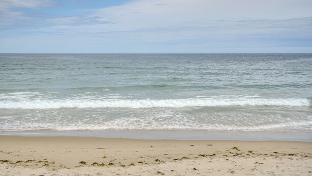 Une plage où les vagues viennent doucement lécher le rivage sous un ciel partiellement nuageux.