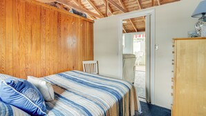 Une chambre avec un plafond en bois, un lit recouvert d’une courtepointe à rayures, une chaise et une armoire en bois.