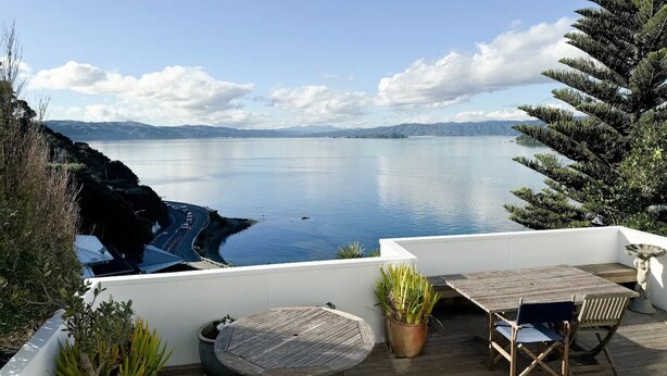Eine Terrasse mit Tisch und Stühlen mit Blick auf ruhiges Wasser und entfernte Berge.
