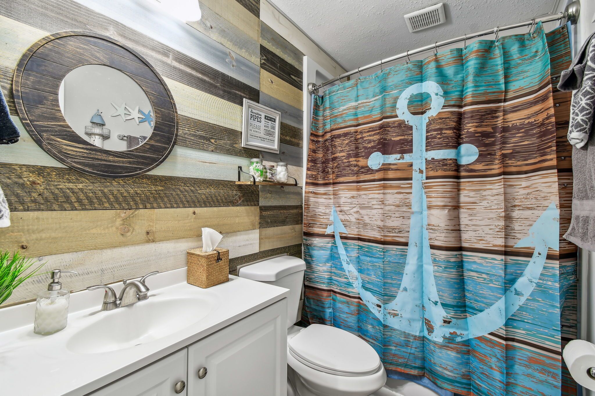 Un baño con cortina de ducha a rayas, un espejo redondo y una pared de madera.