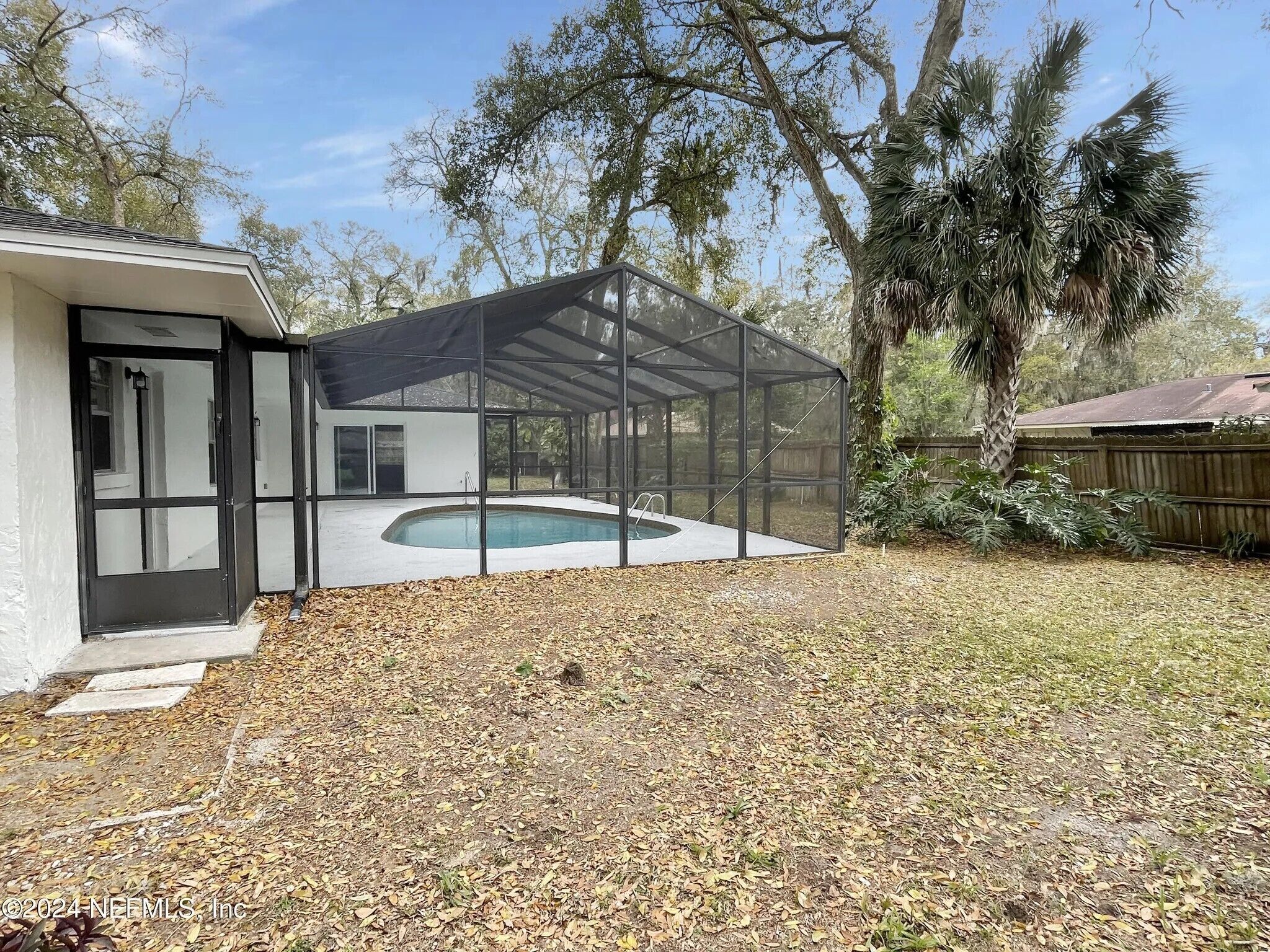 A backyard with a swimming pool, covered patio, and a house with a screened porch.