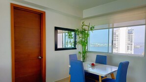 Un comedor con mesa y sillas, una ventana con vista a edificios y agua, y una puerta.
