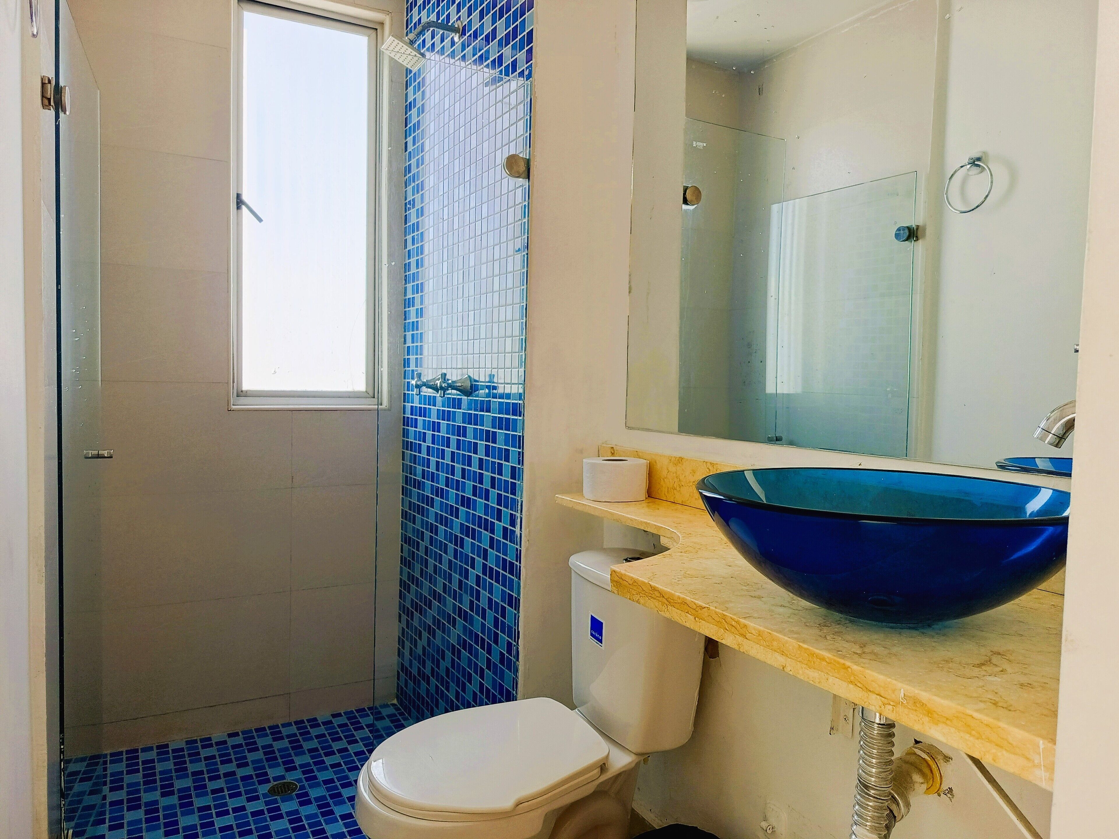 Een badkamer met een blauw betegelde douche, een wit toilet, een wastafel met een blauwe kom en een spiegel boven de wastafel.