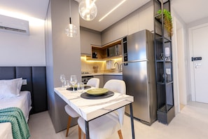 A modern hotel room with a bed, a dining table set with plates and glasses, a kitchen area with a refrigerator and microwave, and a small plant on a shelf. - City House (Barreiras)