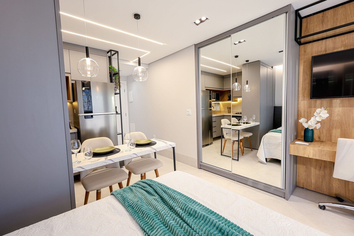 Een moderne hotelkamer met een bed, een zithoek, een keuken en een aan de muur bevestigde televisie.