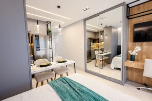 Een moderne hotelkamer met een bed, een zithoek, een keuken en een aan de muur bevestigde televisie.