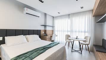 A modern hotel room with a large bed, a desk, and a dining area.