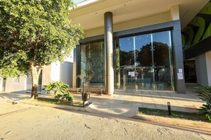 Een modern gebouw met een glazen entree, een grote boom en een bank voor buiten.