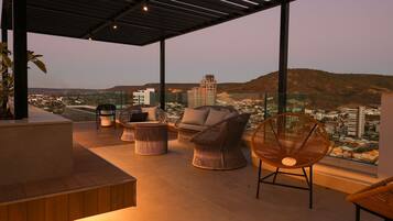 Une terrasse sur le toit offrant une vue sur le paysage urbain, avec un espace salon comprenant des fauteuils en osier et une table ronde.