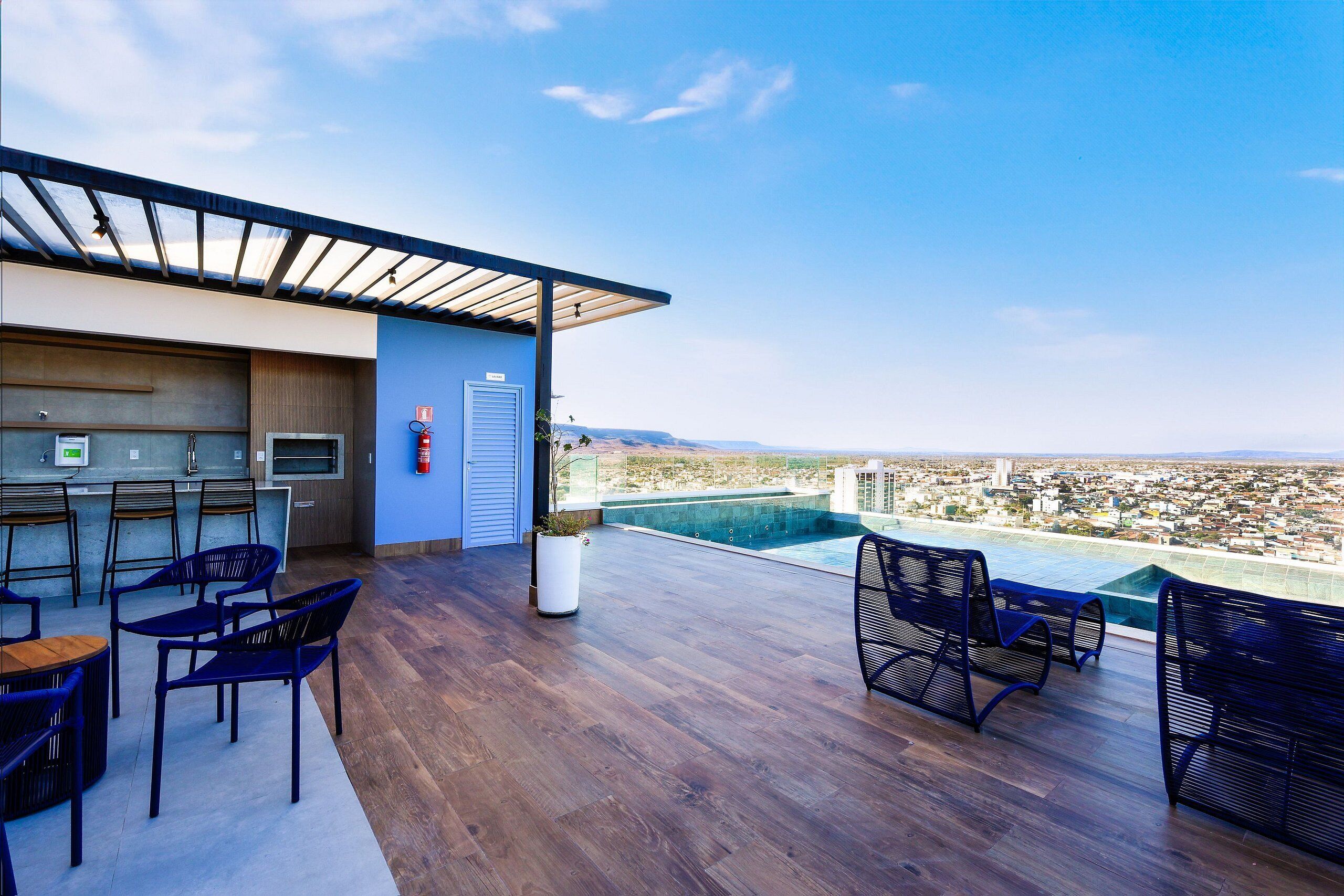 A rooftop bar with wooden flooring, blue chairs, and a city view.
