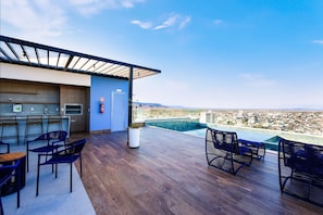 A rooftop bar with wooden flooring, blue chairs, and a city view. - City House (Barreiras)