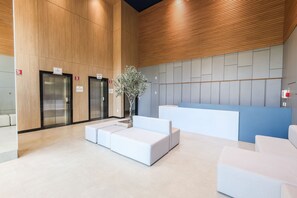 Een modern receptiegedeelte met een receptiebalie, twee liften en een zithoek met een potplant.