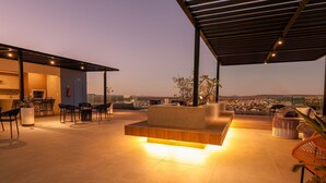 An outdoor patio area with a modern seating arrangement, a kitchen area, and a view of the cityscape. - City House (Barreiras)