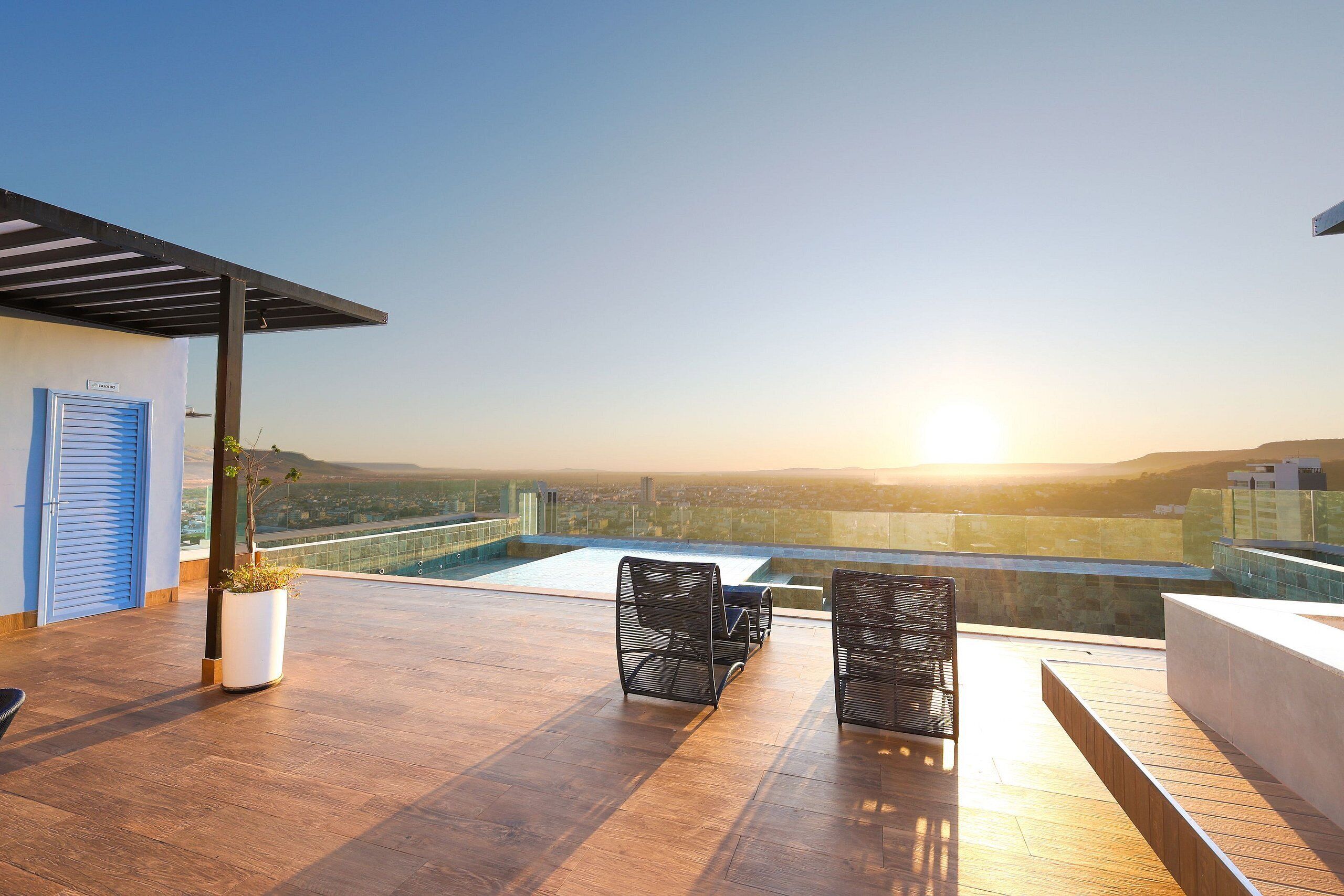 A rooftop terrace with two chairs, a potted plant, and a view of the cityscape at sunset.