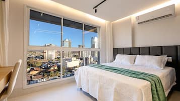 A modern bedroom with a large window, a bed with white bedding, and a view of the cityscape.