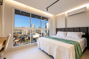 A modern bedroom with a large window, a bed with white bedding, and a view of the cityscape. - City House (Barreiras)