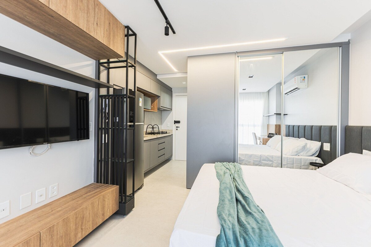Een moderne hotelkamer met een bed, een televisie, een houten kast, een kitchenette en een schuifdeurkast.