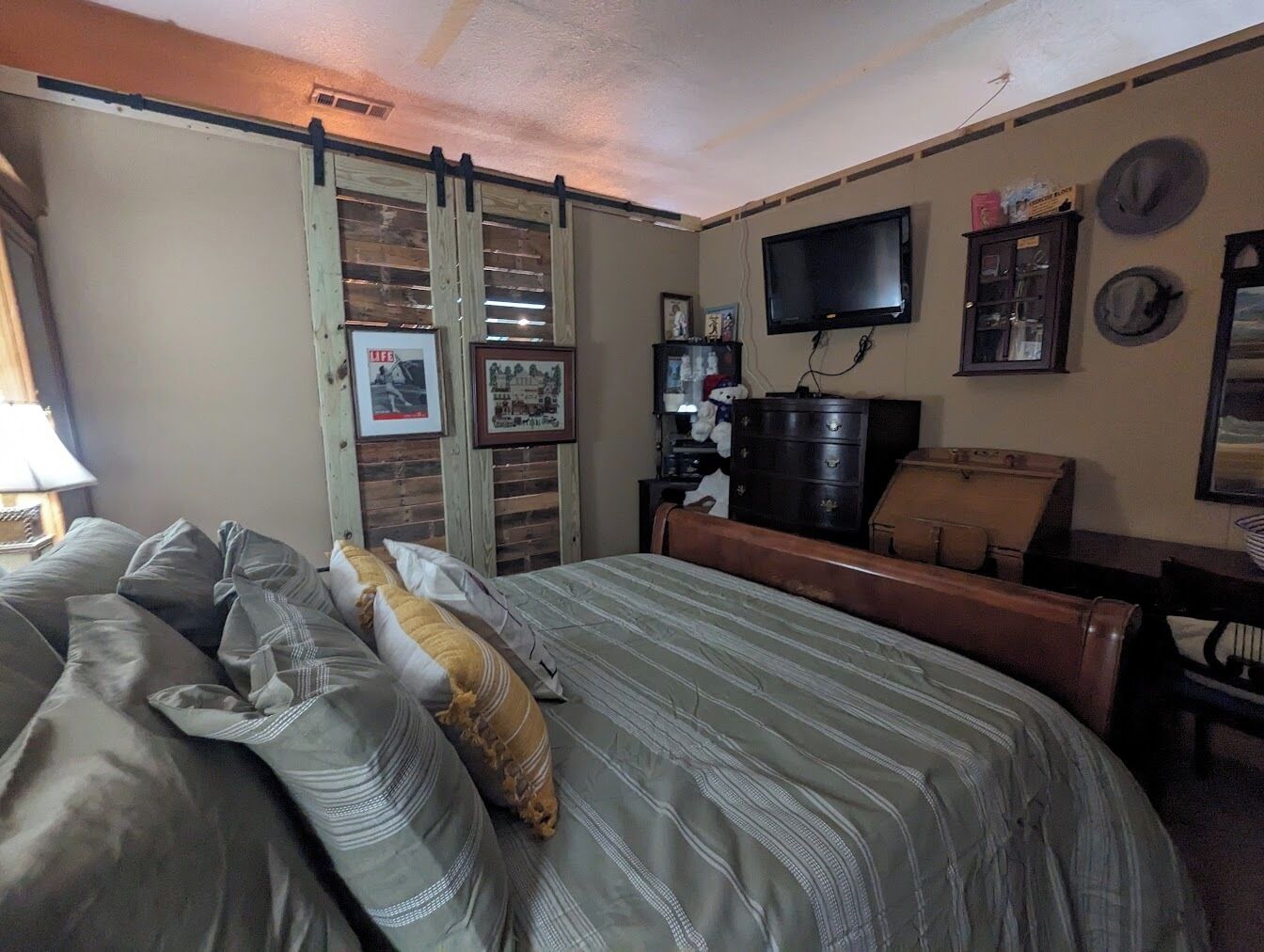 A bedroom with a bed, a dresser, a television, and various wall decorations.