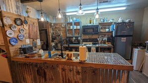 A rustic kitchen with a wooden bar counter, hanging light fixtures, and various kitchen appliances. - 1-bedroom/bath Cozy rustic cottage, off the RCR with AC in lovely Wrinkler, Tx.  (Streetman)