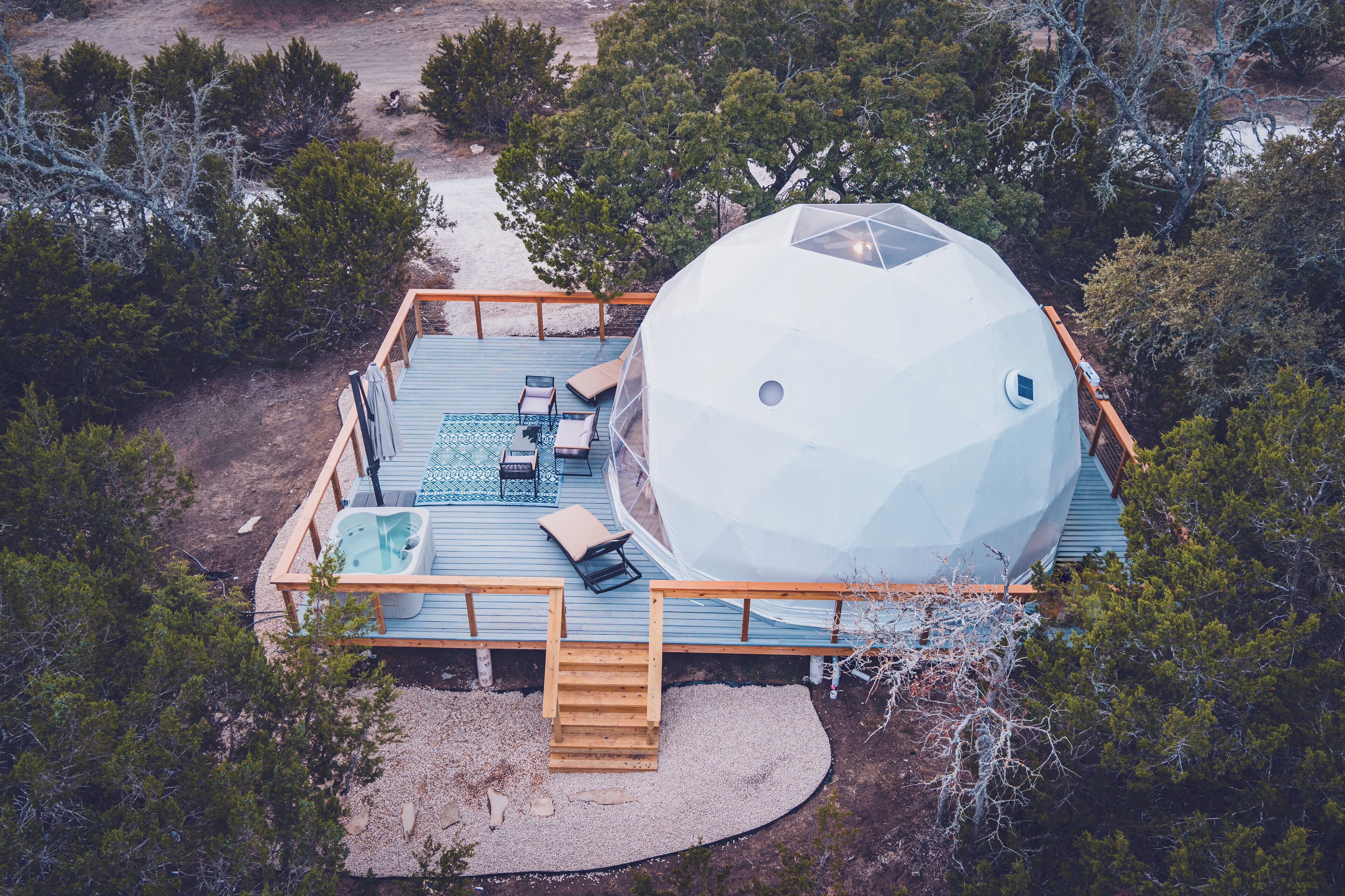 Una estructura de domo geodésico con terraza, asientos exteriores y una bañera de hidromasaje.