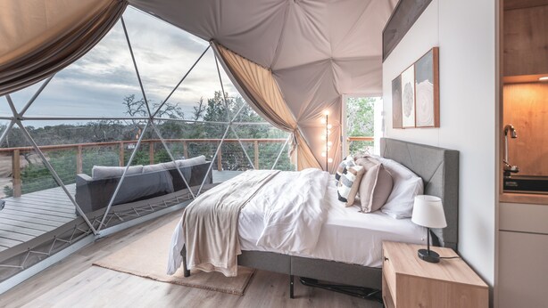 A bedroom with a bed, bedside table, and a view of the outdoors.