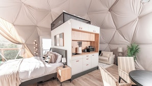 A cozy bedroom with a bed, bedside table, and a kitchenette area with cabinets and a sink.