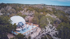 A dome-shaped accommodation with a deck, surrounded by dense forest.