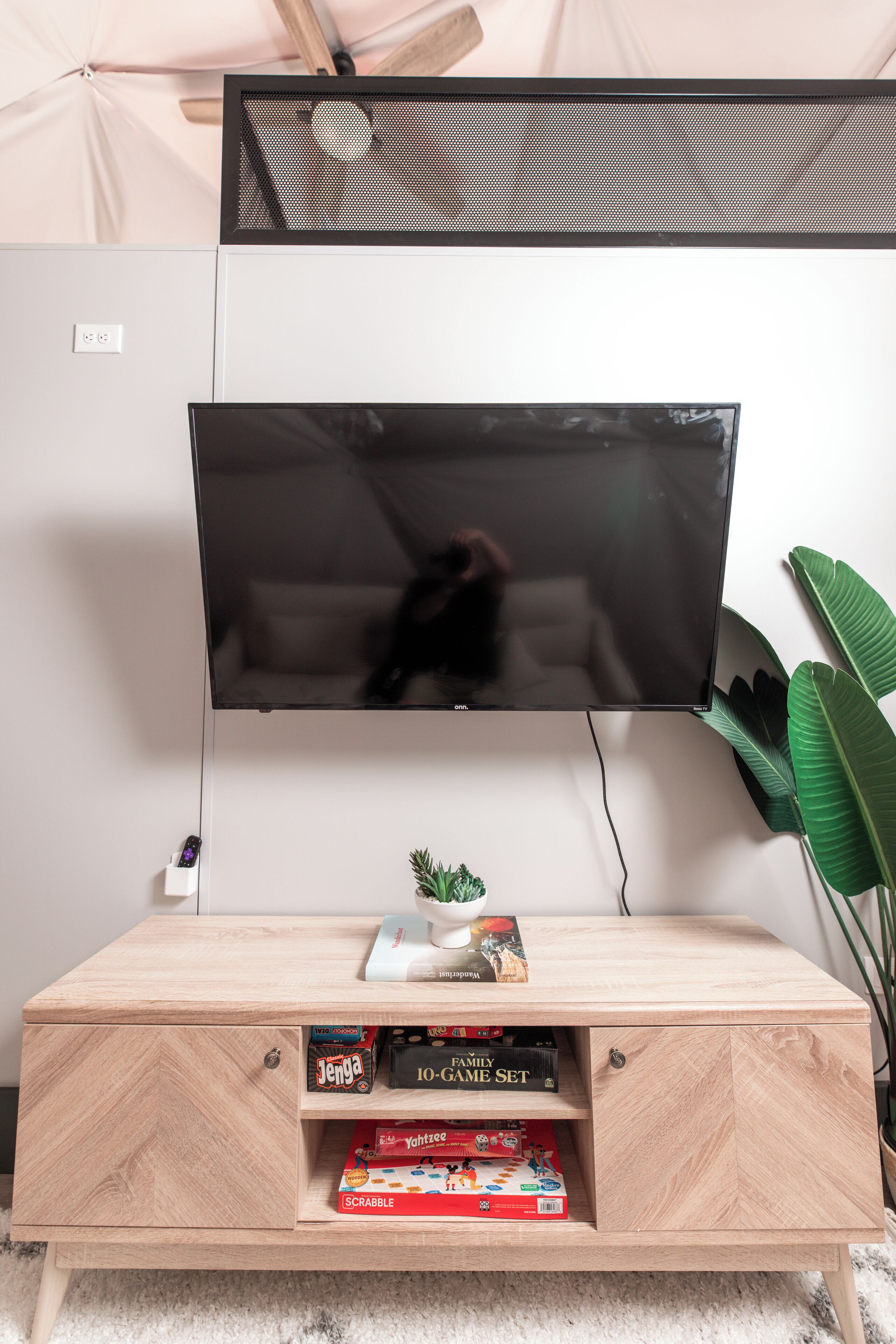 A flat-screen TV mounted on a wall above a wooden TV stand with shelves holding board games.