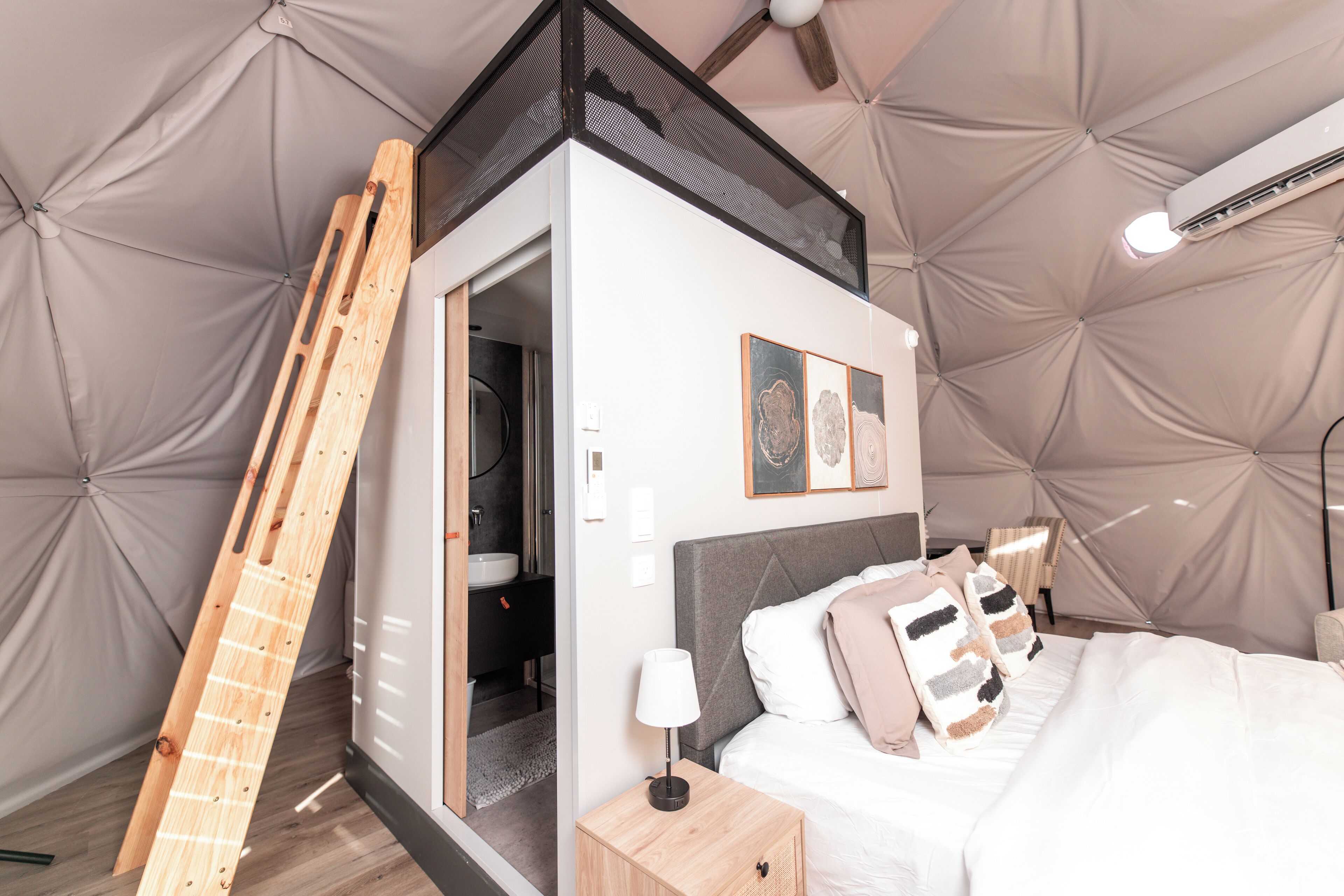 Un dormitorio con cama, mesita de noche, lámpara y una escalera apoyada en la pared.