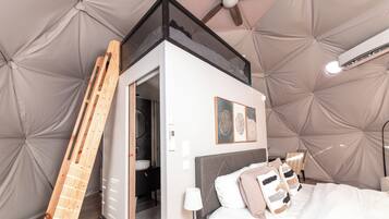 Un dormitorio con cama, mesita de noche, lámpara y una escalera apoyada en la pared.