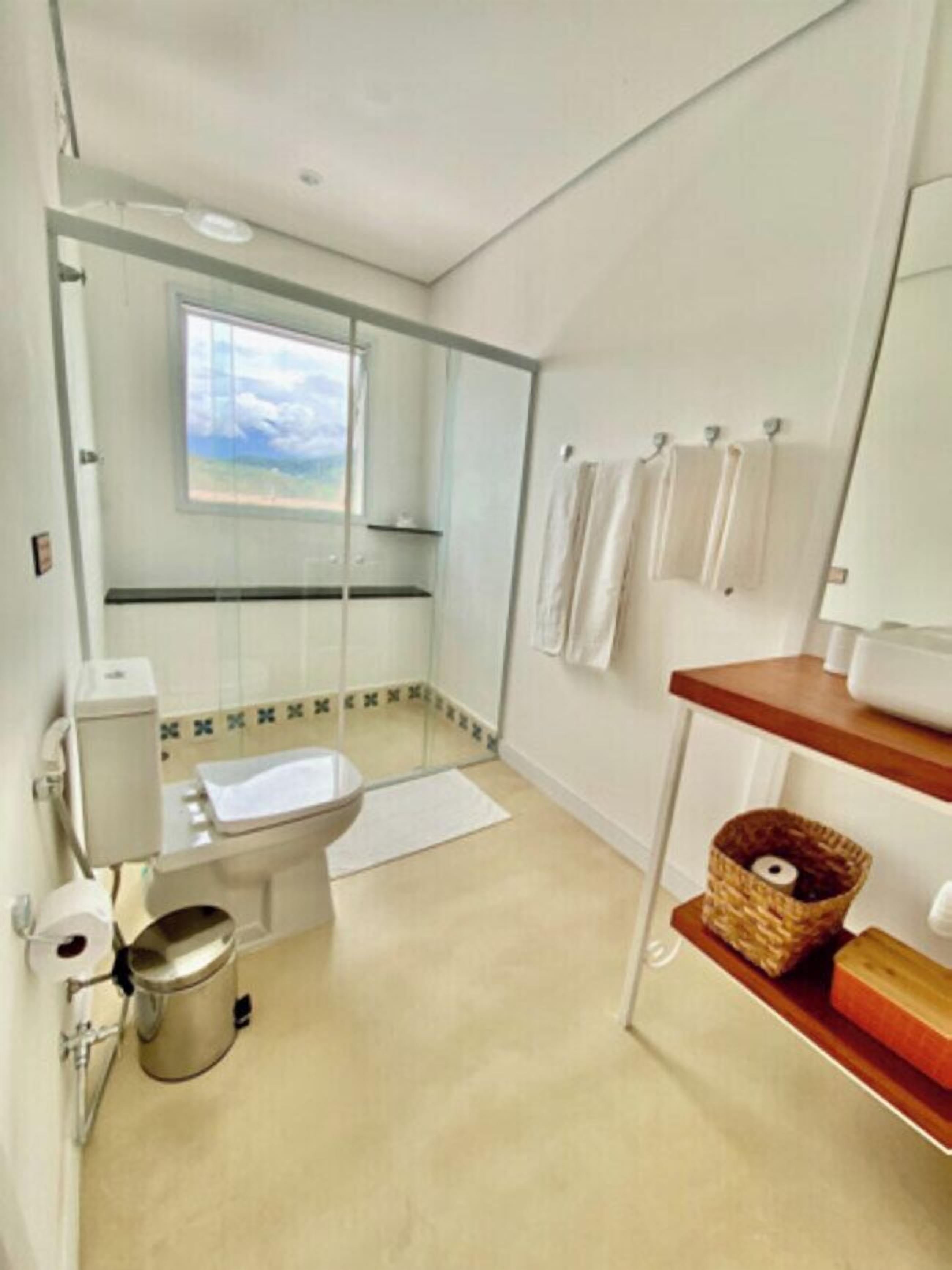 A modern bathroom with a toilet, bidet, and a glass shower enclosure. There is a window with a view of the sky, and a shelf with towels and a basket.
