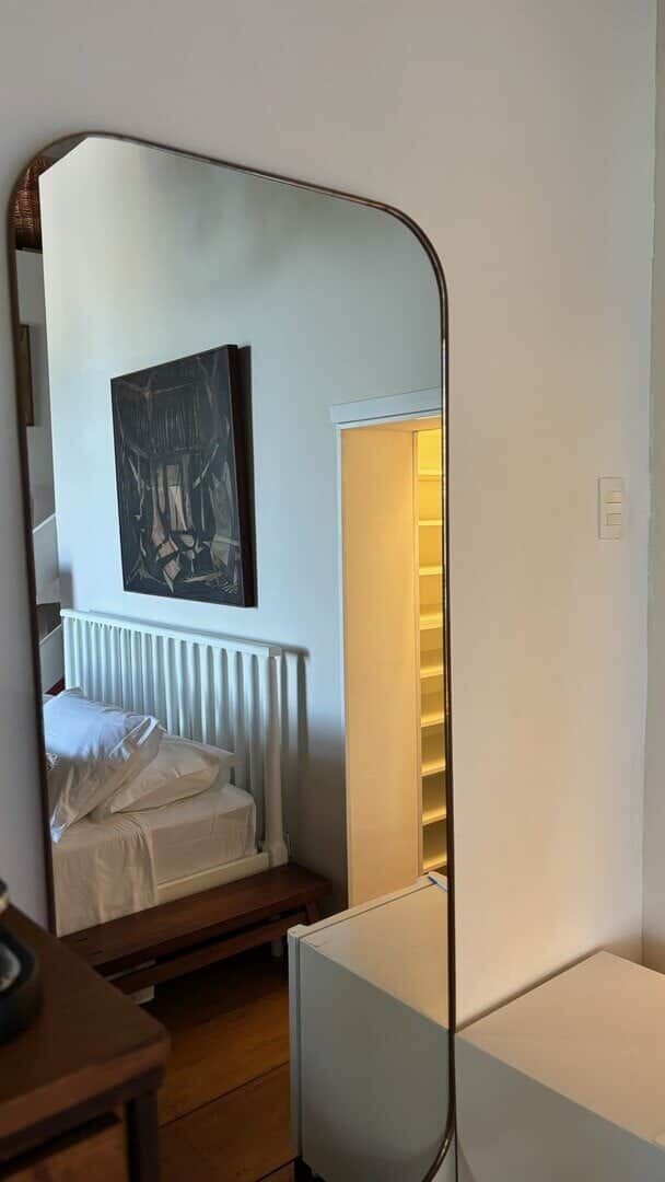 A bedroom with a bed, a bedside table, a mirror, and a painting on the wall.