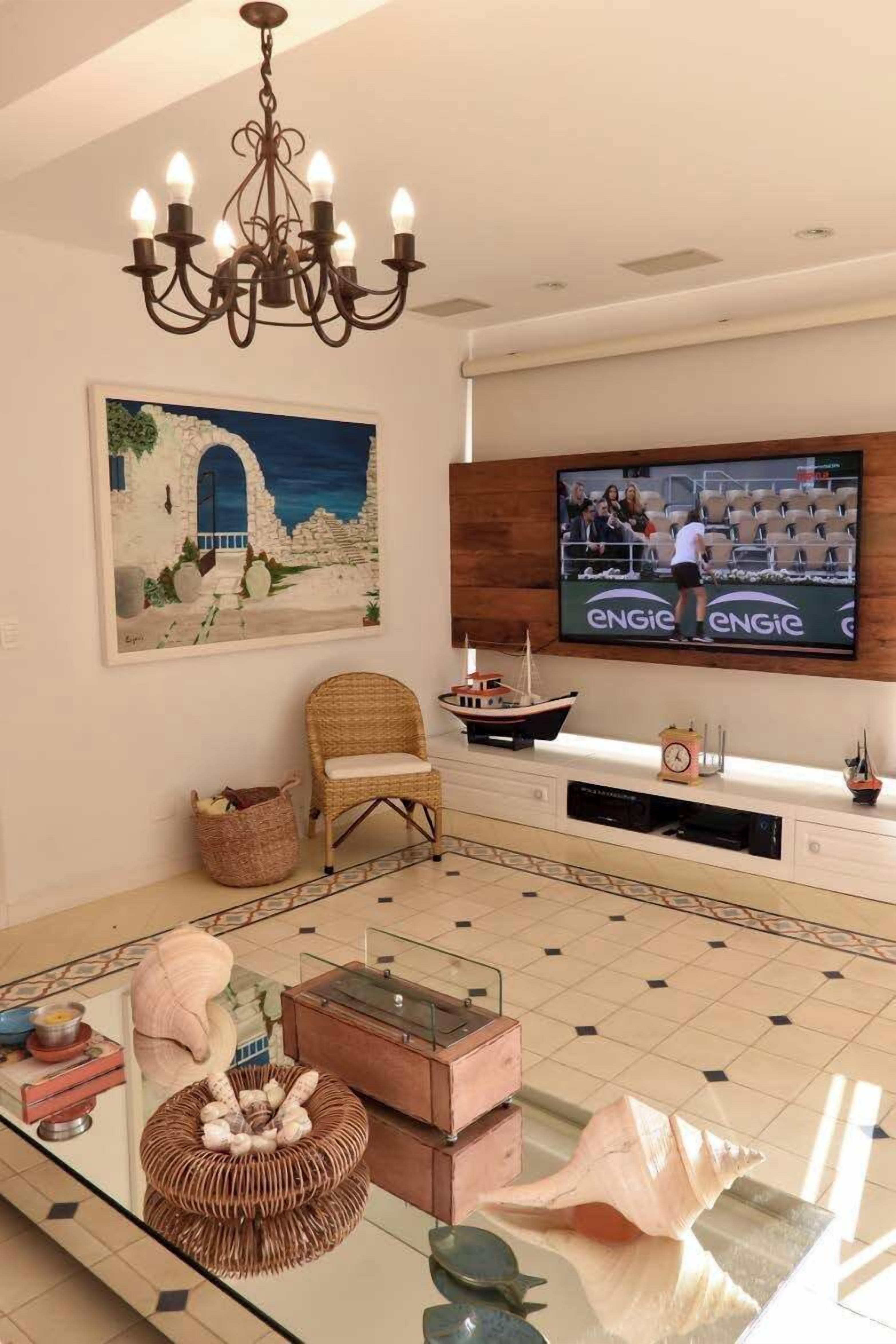 A living room with a television, wicker chair, decorative shells, and a chandelier.
