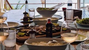 A dining table set with various dishes, glasses, and condiments, overlooking a scenic view of mountains and the sea. - Villa Dei Fiori (São Sebastião)