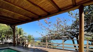 A pool area with a wooden deck, a covered seating area, and a view of the sea. - Villa Dei Fiori (São Sebastião)