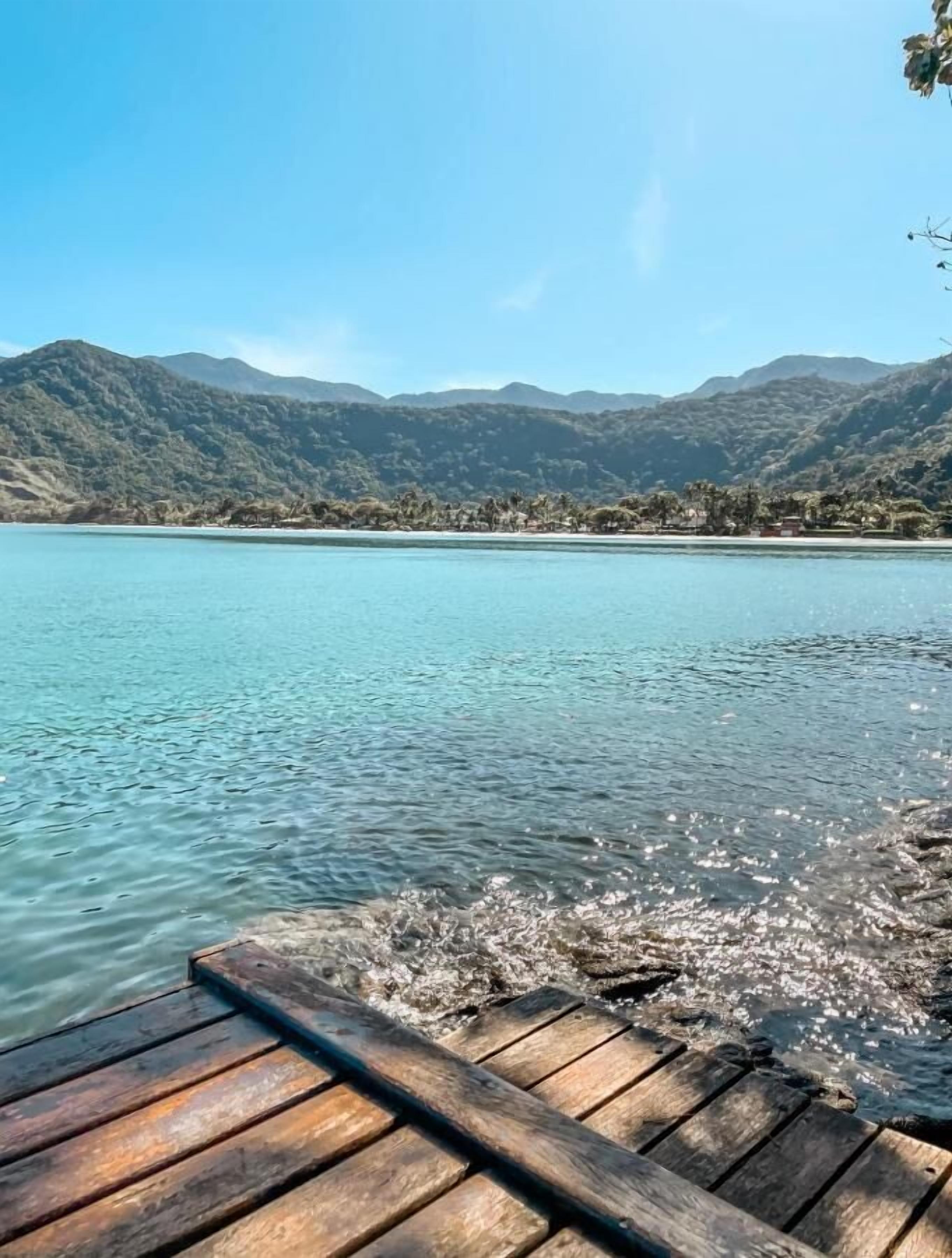 A wooden dock extending into a clear lake with mountains in the background.