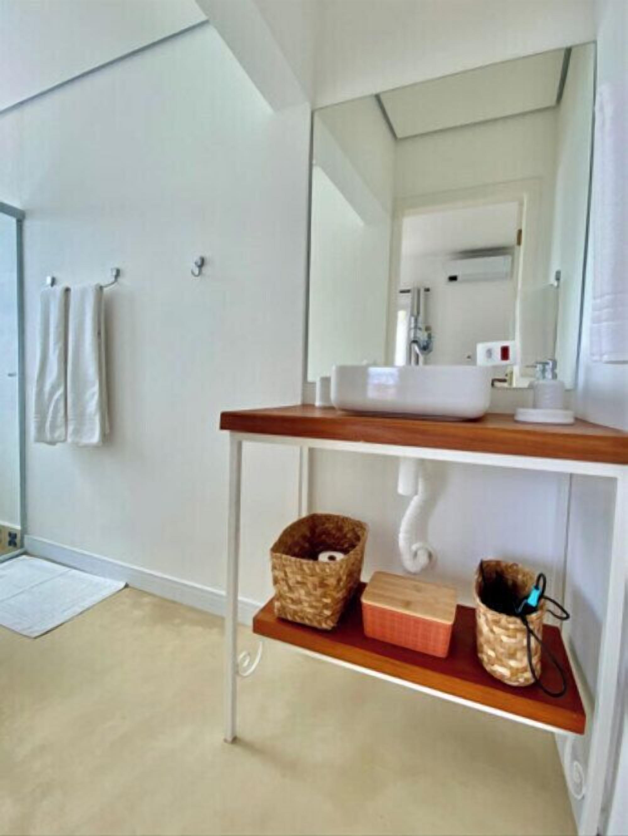 A bathroom with a white sink, mirror, and wooden vanity. There are two baskets on the vanity and a towel rack on the wall.